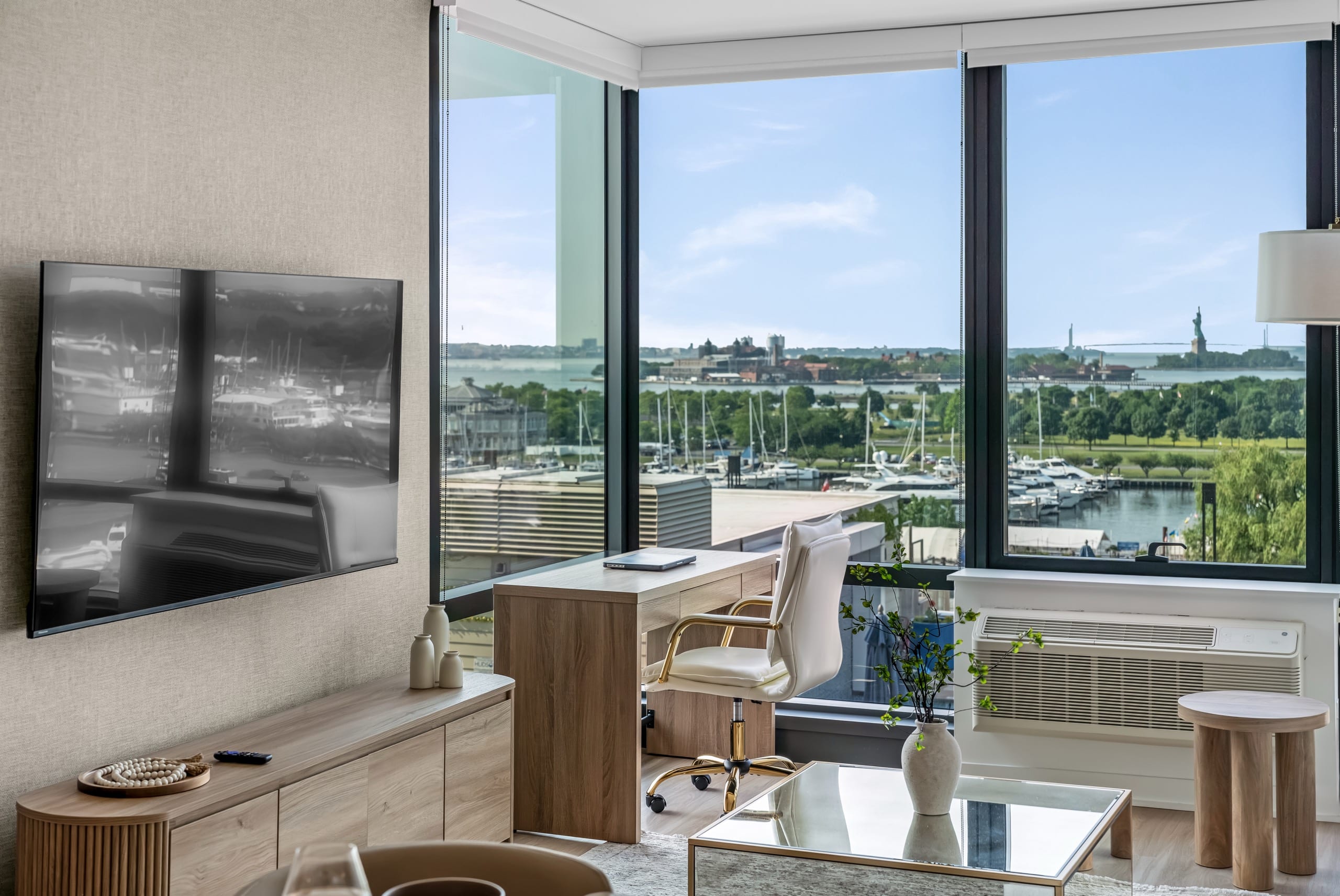 A desk beneath floor-to-ceiling windows in a World Class residence, looking across the marina to the Statue of Liberty