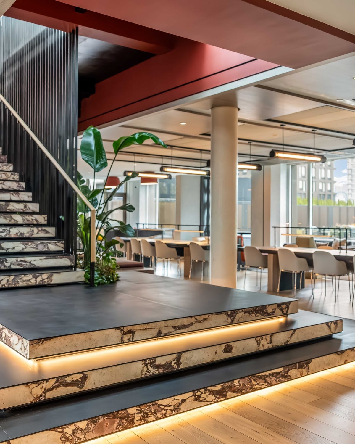 An attended building lobby with a marble staircase, warm lighting and planted terraces