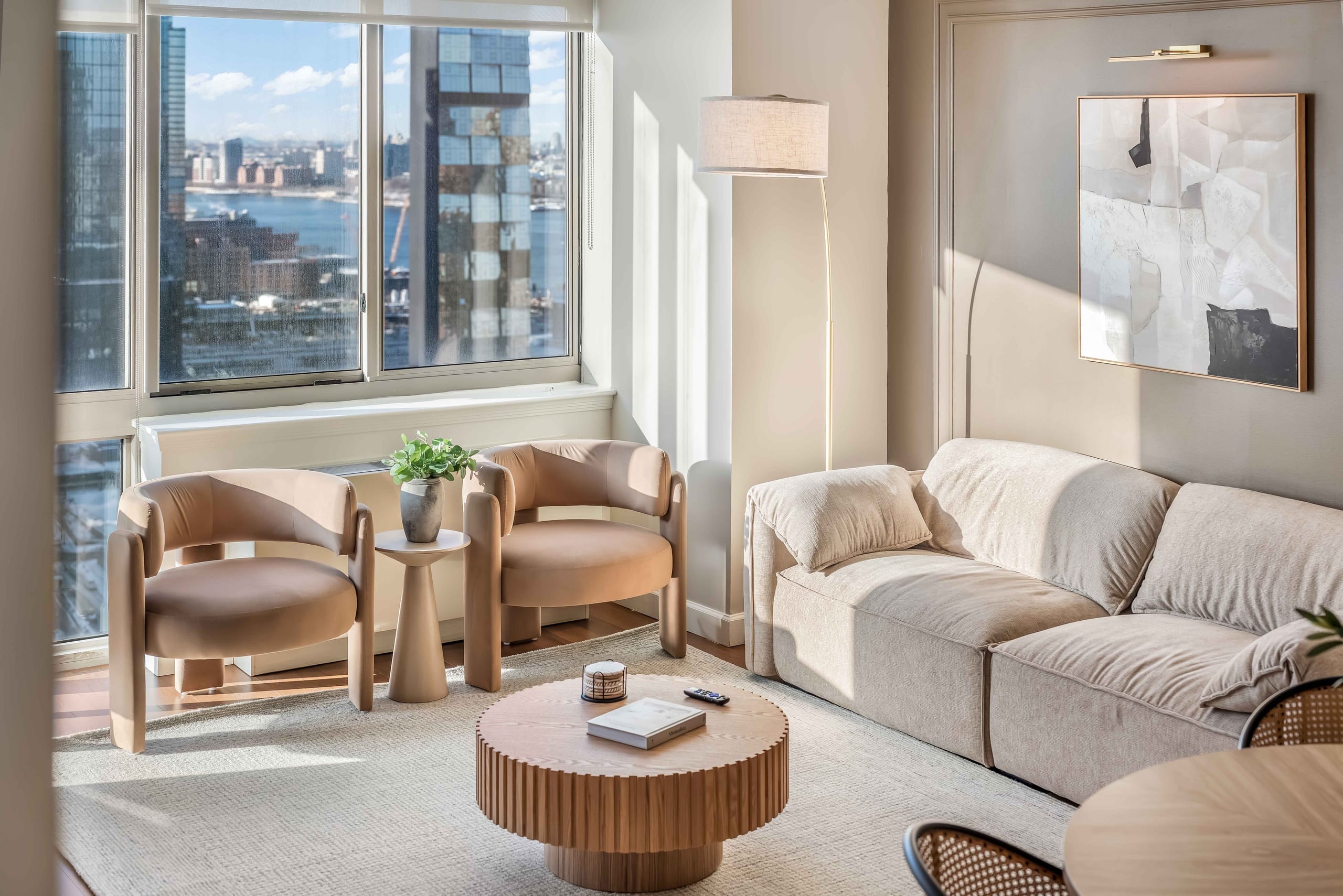 A bright World Class® living room with tan armchairs and a fluted low table, the river visible through full-height windows
