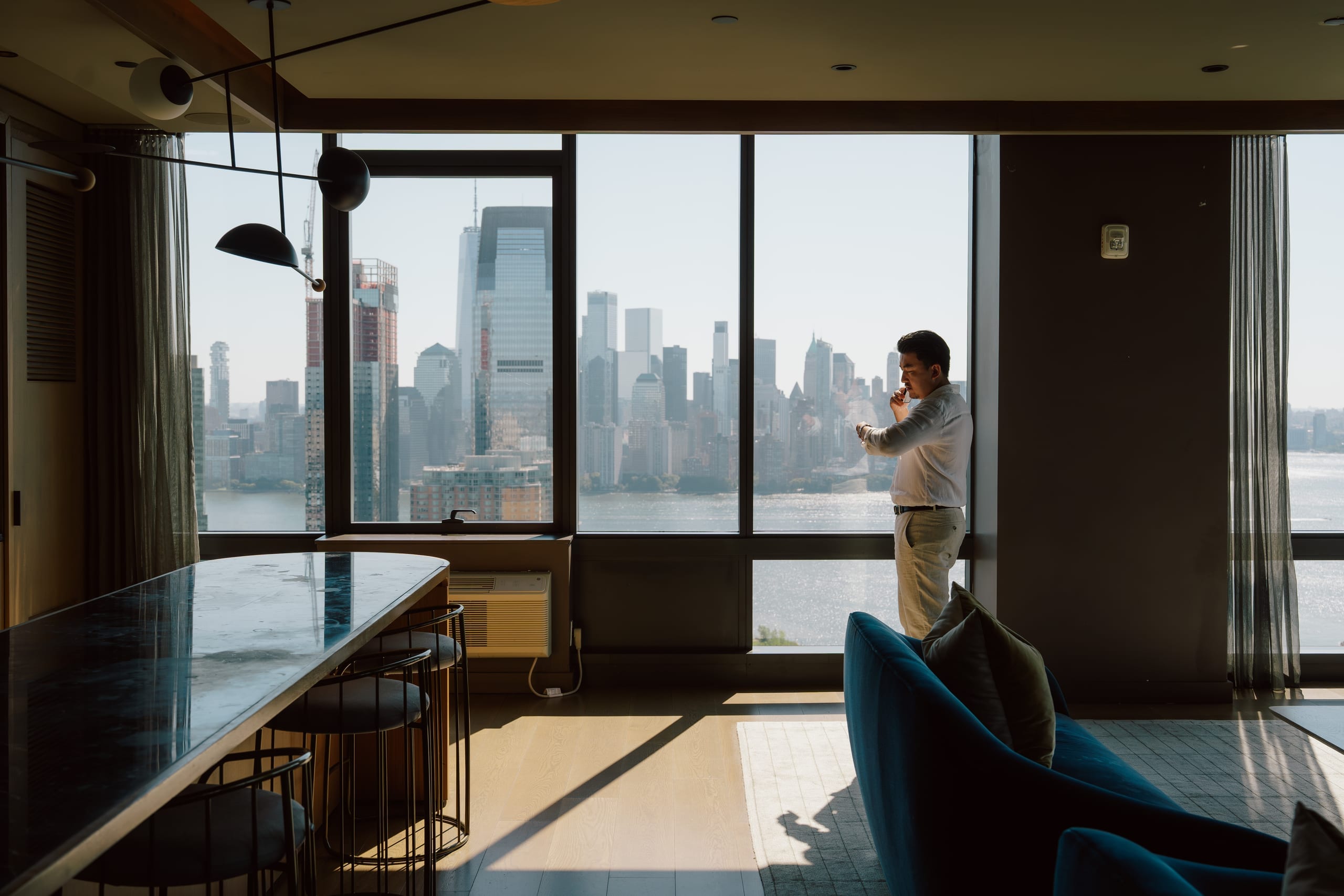 A resident standing at the window of a World Class residence, the Manhattan skyline across the water beyond