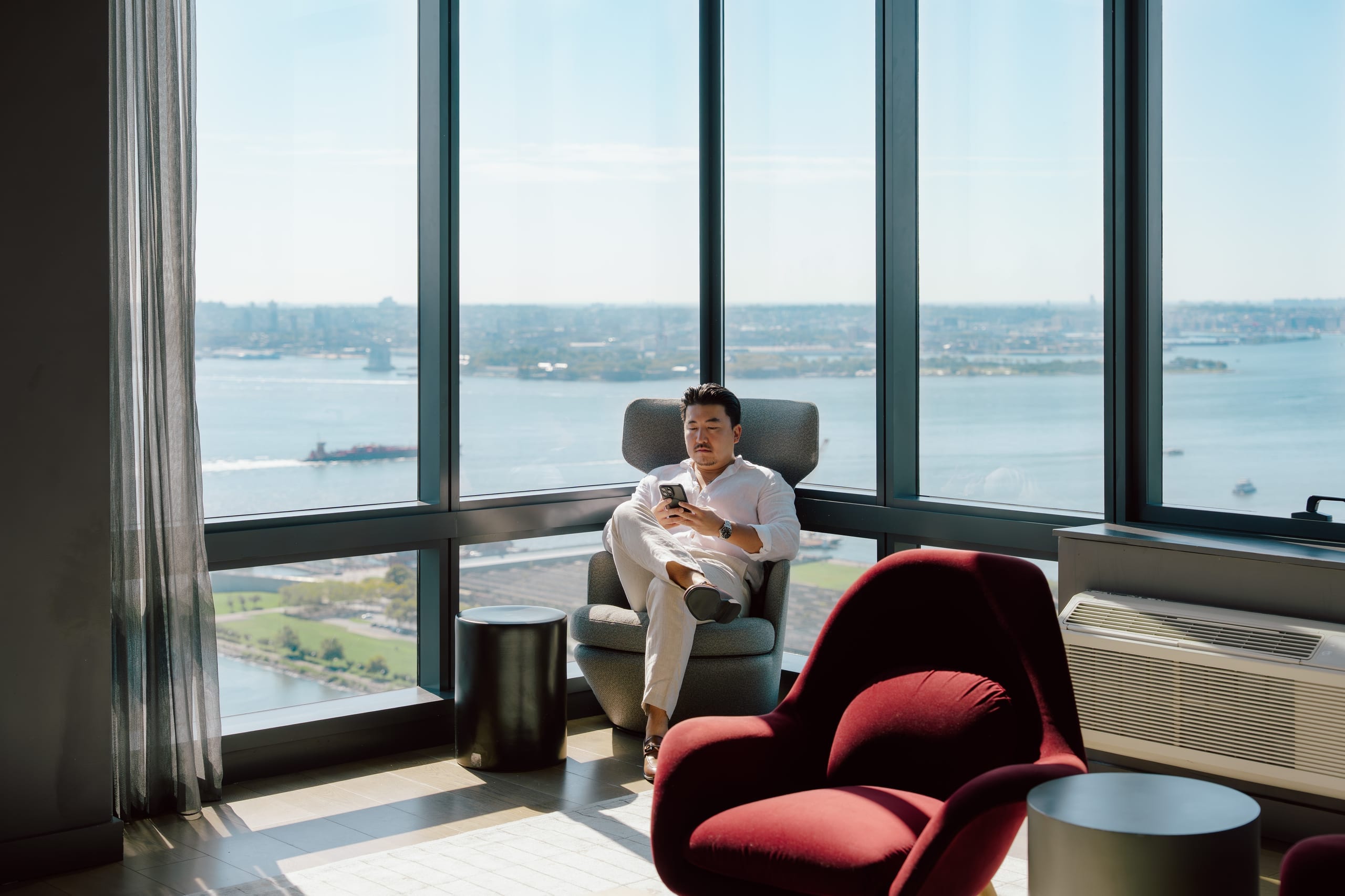 A resident seated by floor-to-ceiling windows in a World Class residence, the Hudson river stretching out below