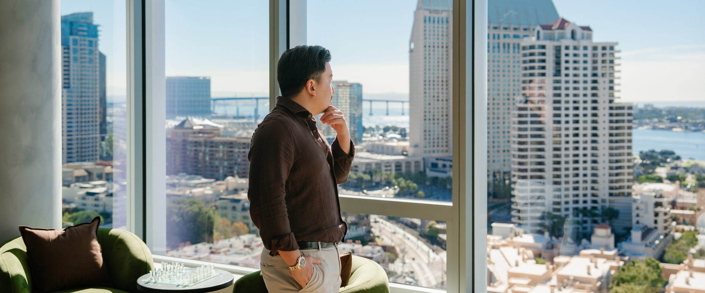 A resident at the floor-to-ceiling window of a World Class residence, looking out over the downtown skyline and bay