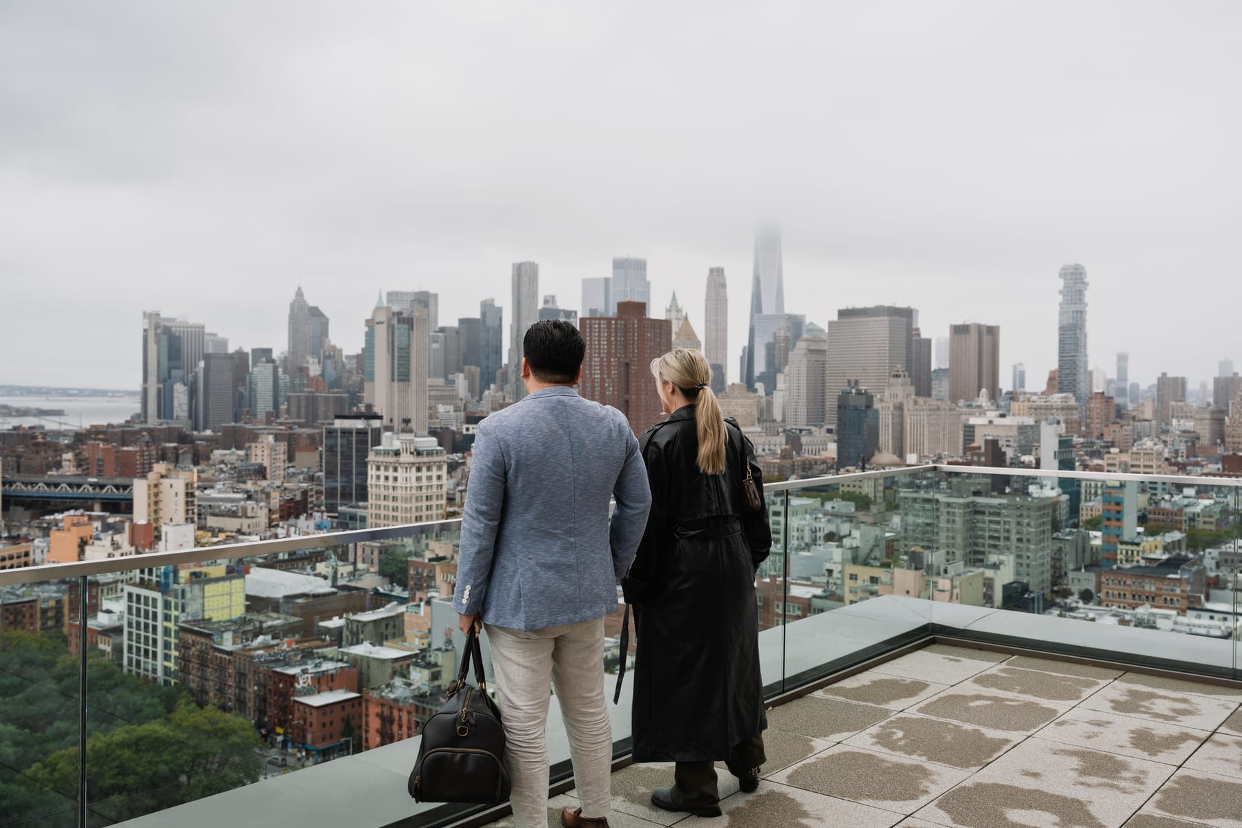 Two residents with luggage at a rooftop railing, taking in the Manhattan skyline on the day they arrive