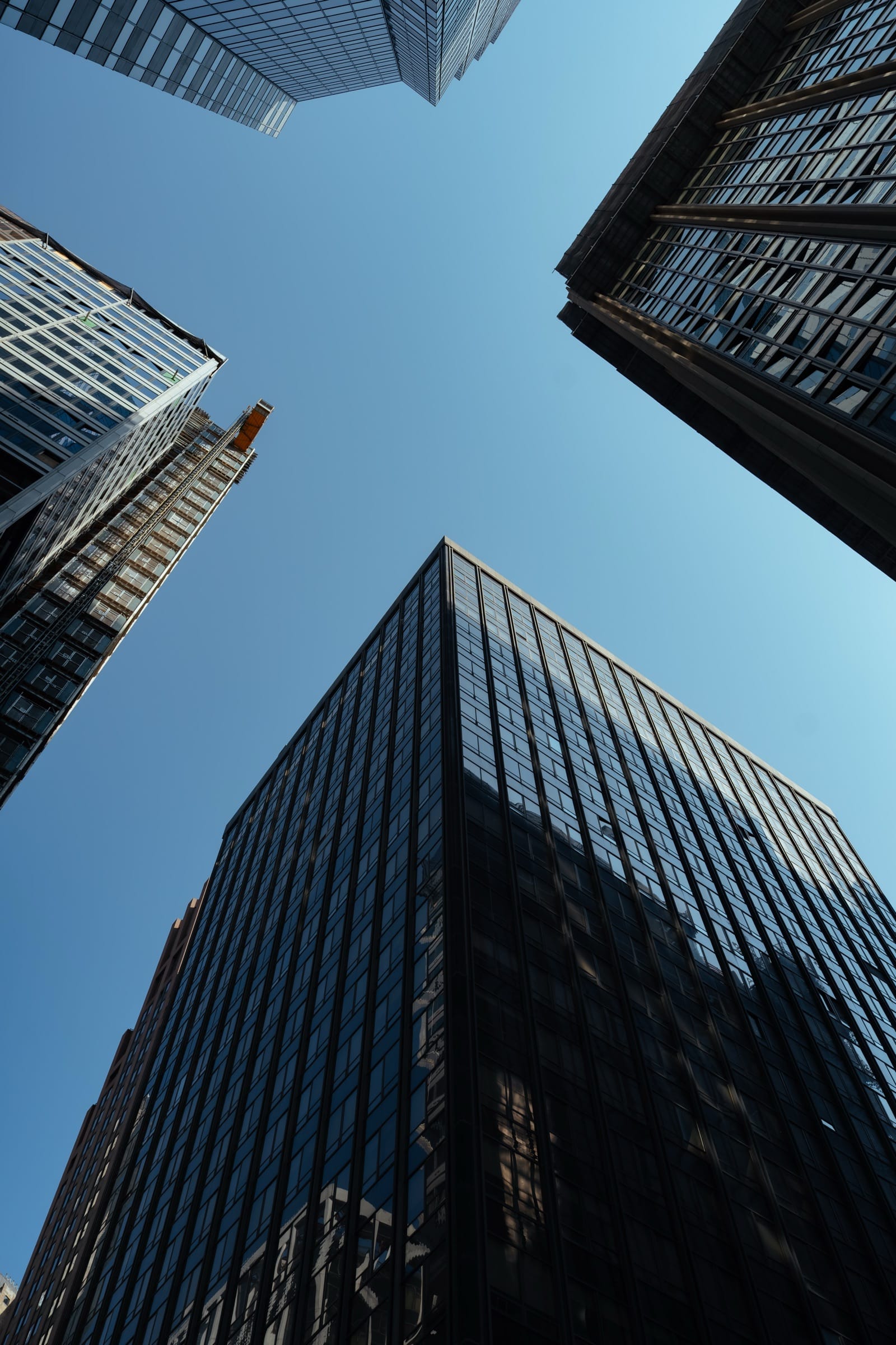 Glass and steel towers in the Financial District seen looking straight up from the street, converging against a clear sky