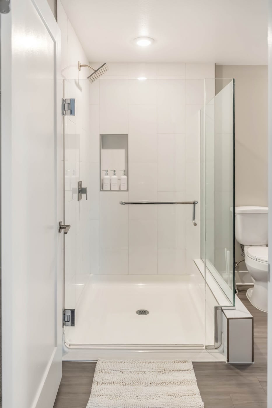 A walk-in glass shower in a World Class residence, with a rain head and bath essentials set in a tiled niche
