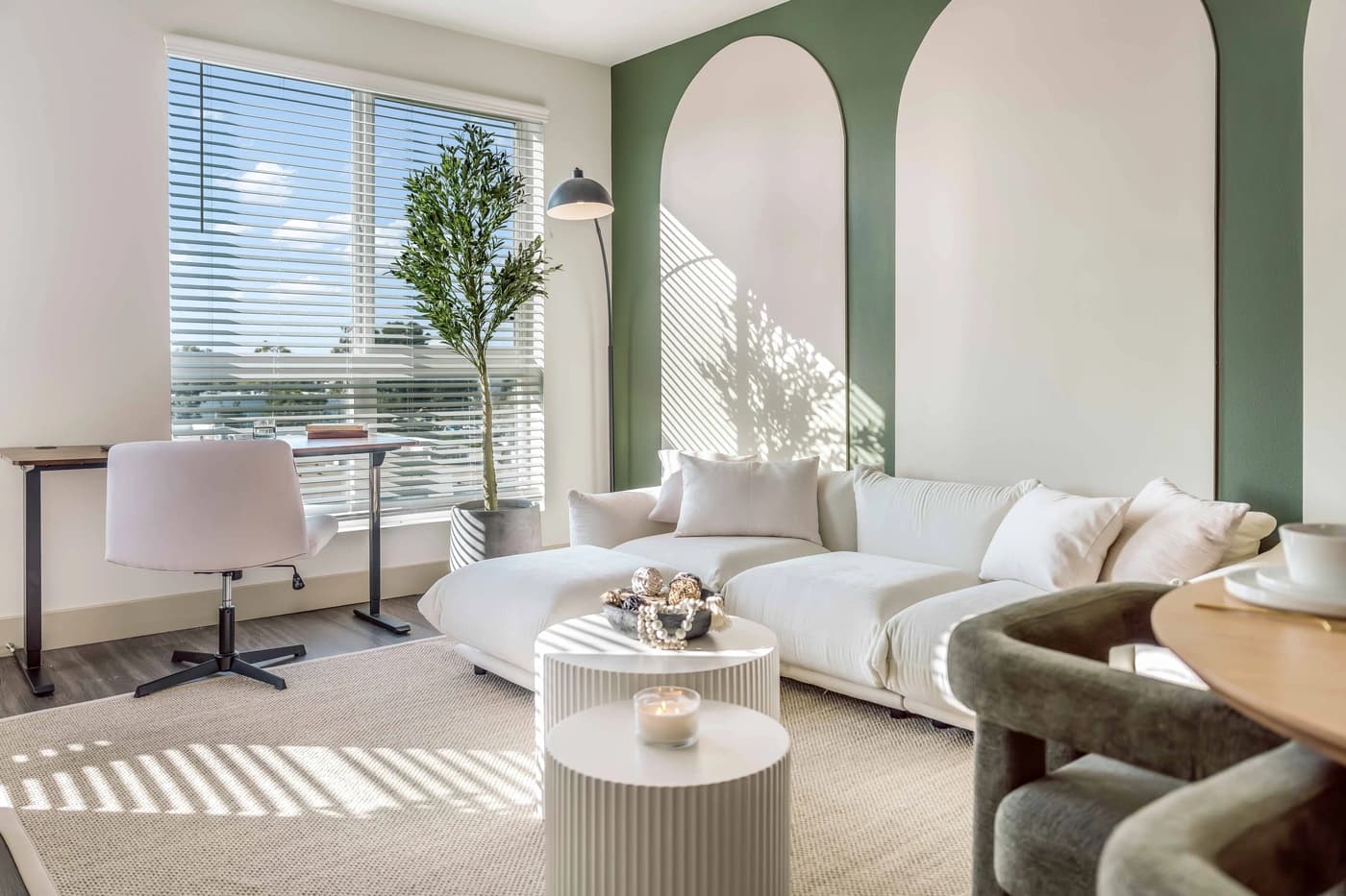 White living room sofa beside desk and green wall with rounded accents at Casa Tivoli by World Class® in Irvine