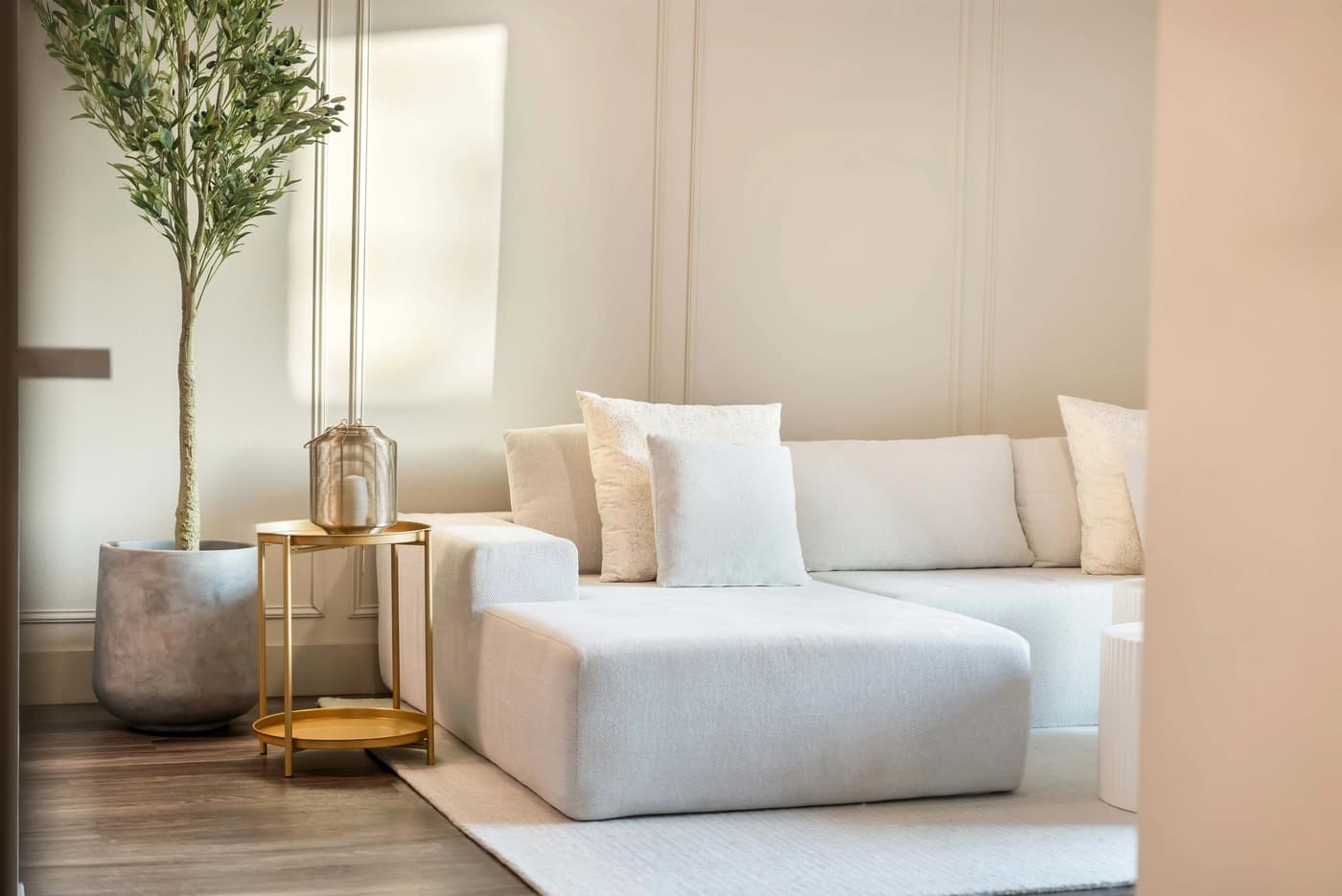 White sectional sofa beside tall plant and round gold-colored side table at The Madisen by World Class® in Irvine