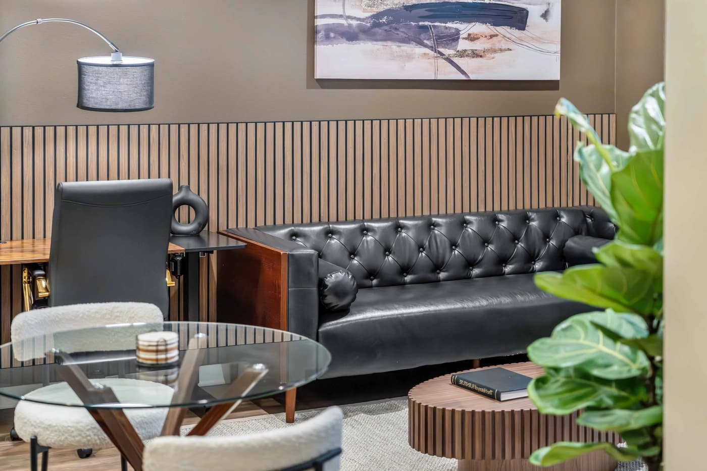 Black tufted sofa and desk chair beneath abstract painting and vertical wall slats at Casa Vincente by World Class® in Irvine