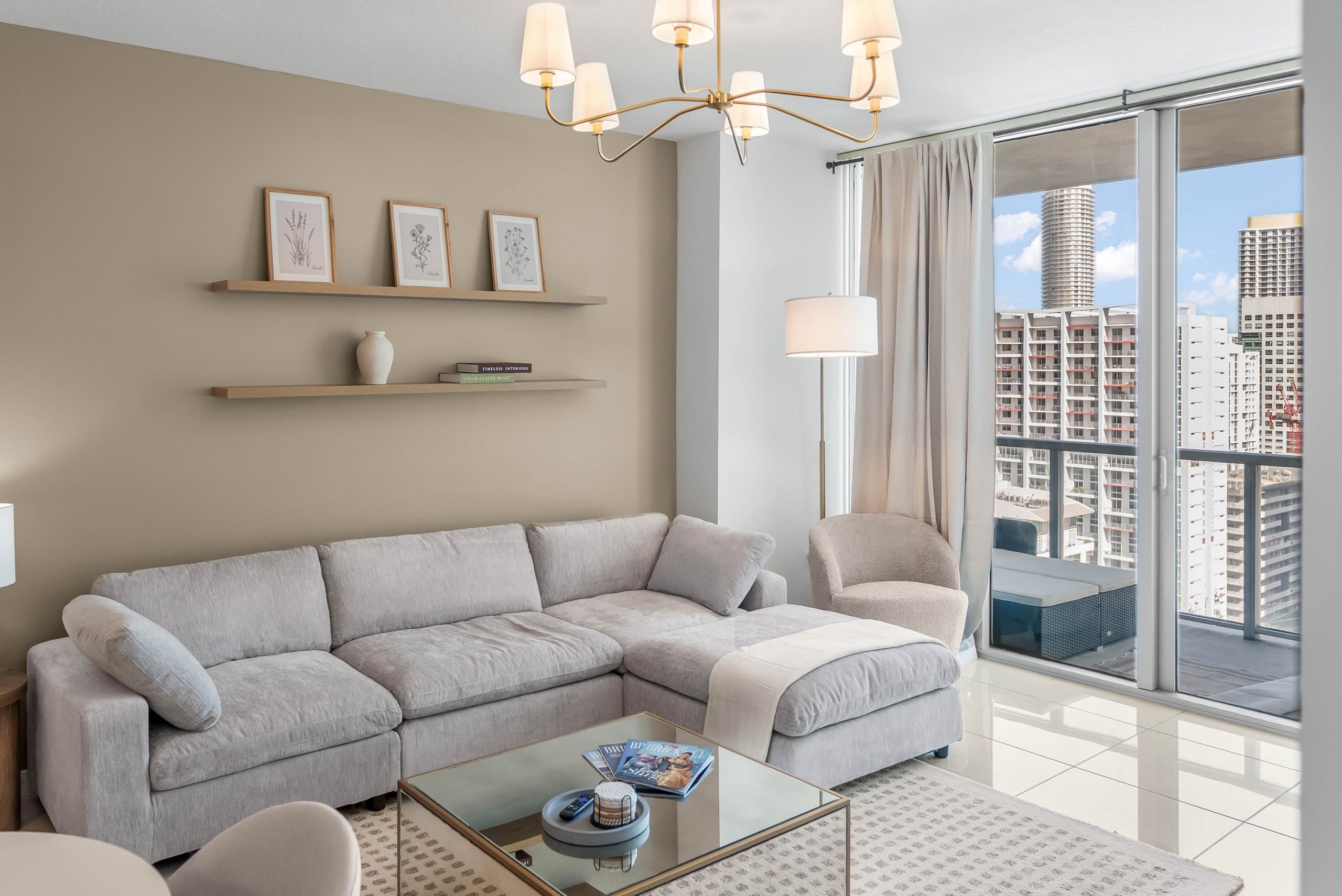 Gray sectional sofa beneath display shelves beside glass table and balcony doors at The Oasis in Miami