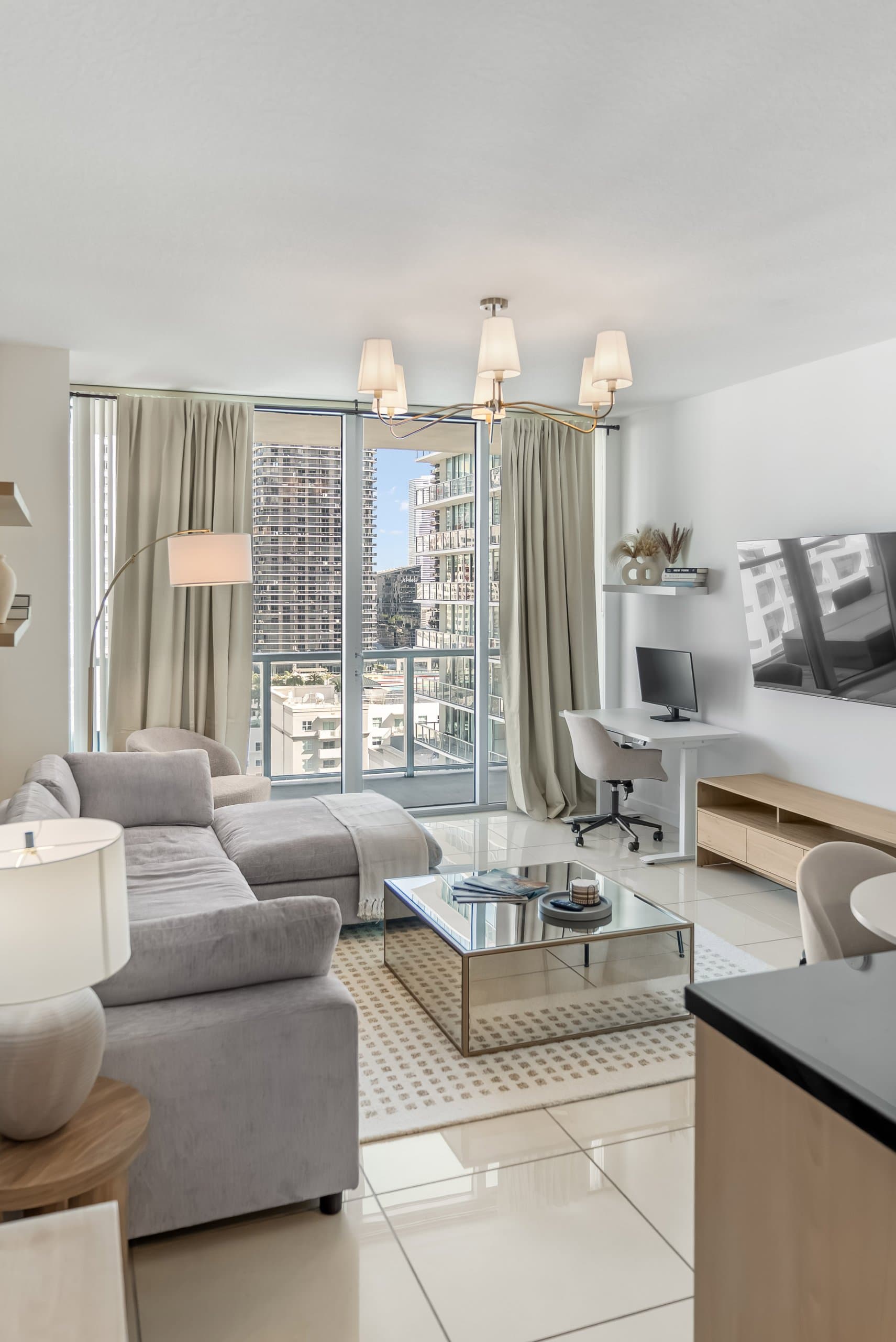 Living room seating around reflective coffee table beside windows and balcony door at The Oasis by World Class® in Miami