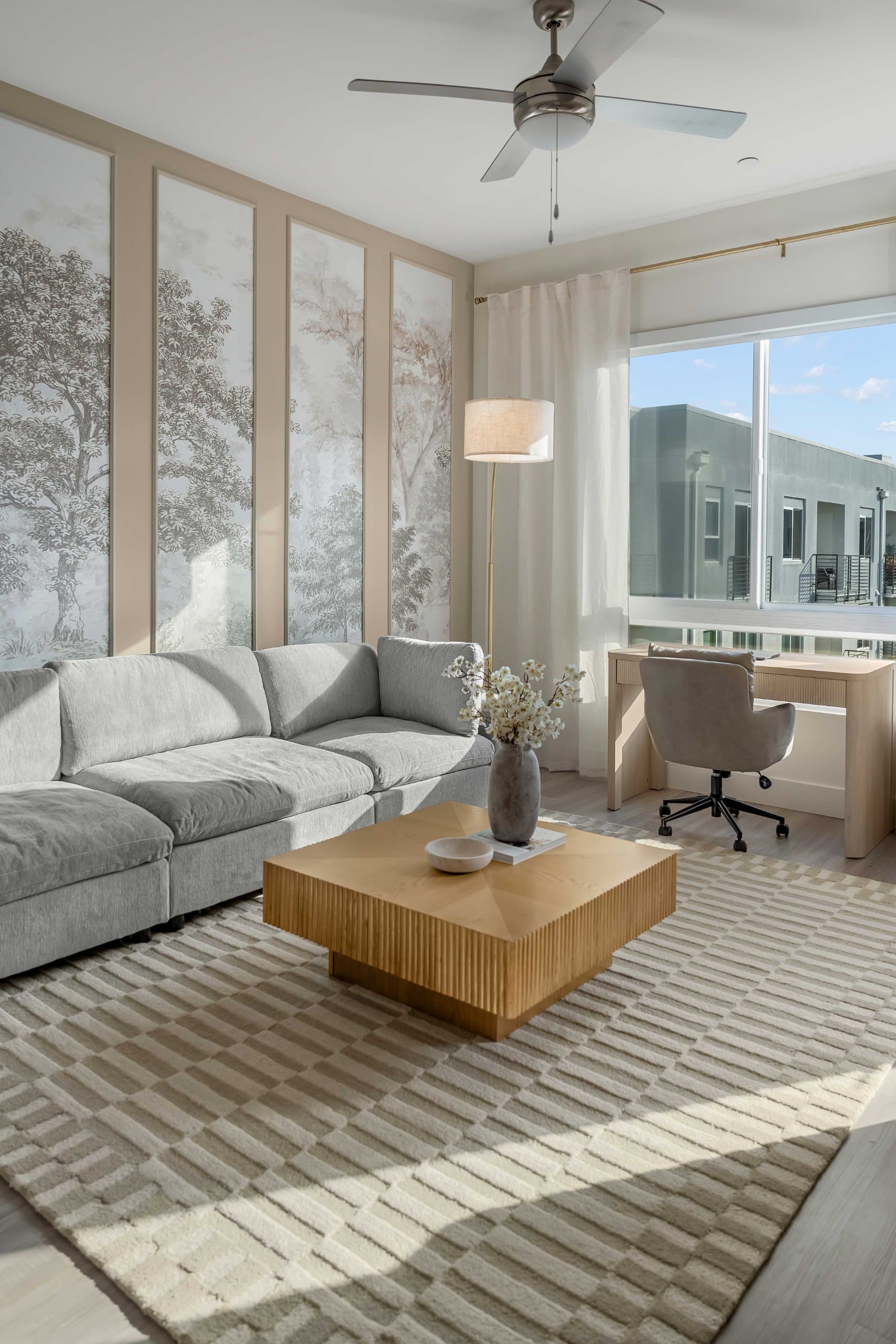 Living room sectional and coffee table beside desk beneath ceiling fan at The Seraphina by World Class® in Newport Beach